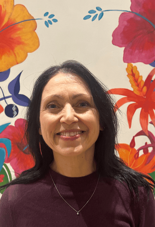 Dark haired woman standing in front of painted flowers.